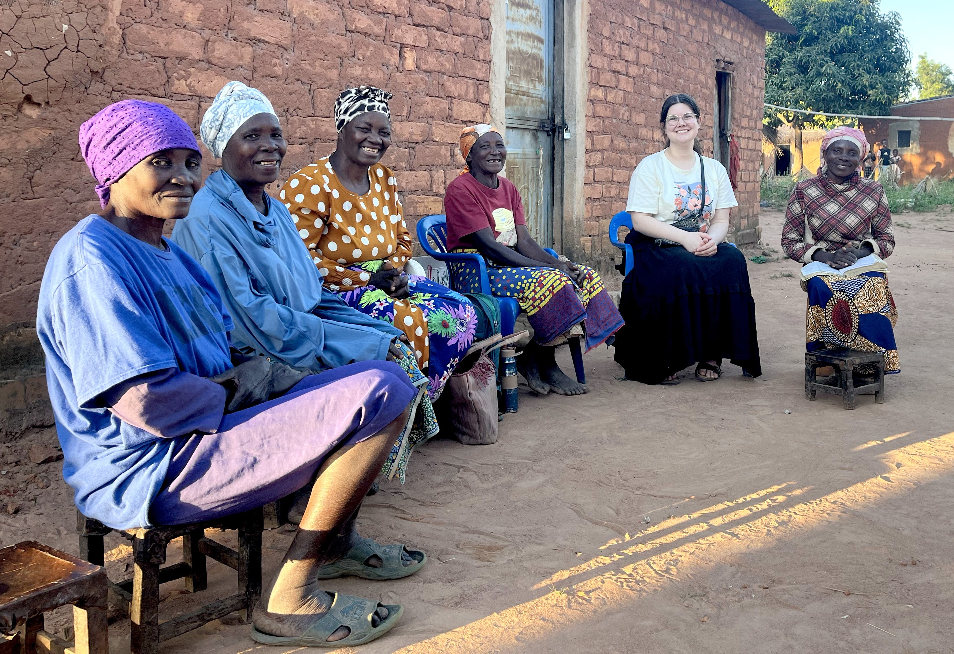 During an Immersion 15 assignment, a young adult participant spends time with local community members outside a village home, building relationships and learning from the people and culture through shared conversation.